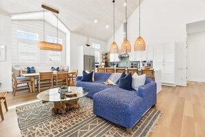 Uma sala de estar ampla com um sofá seccional azul, uma mesa de centro de vidro e um espaço de jantar com cadeiras e mesa de madeira.