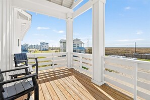 Um deck coberto com grades brancas, uma piscina e casas ao fundo.