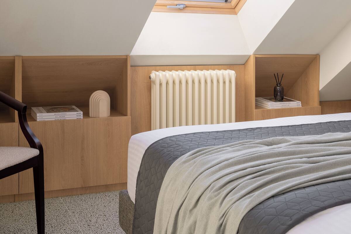 A bedroom with a skylight, a radiator, and a bed with a quilted cover.