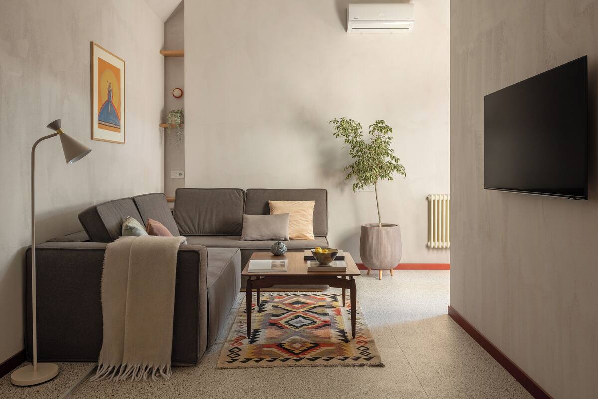 A modern living room with a gray sofa, a coffee table, a potted plant, a floor lamp, and a flat-screen TV.