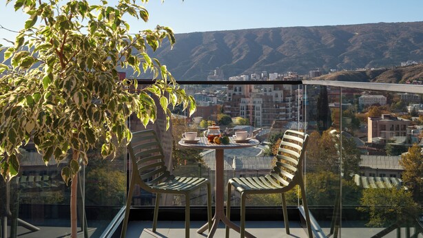 Un balcón con mesa y sillas, con vistas a un paisaje urbano y colinas.