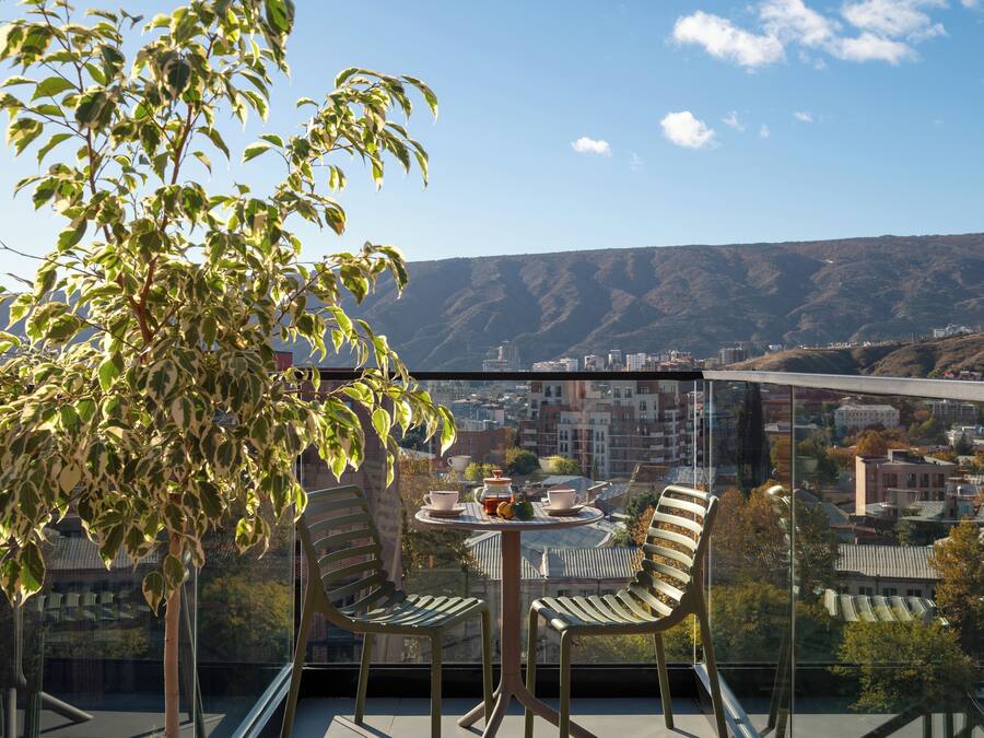 A balcony with a table and chairs, overlooking a cityscape and hills.