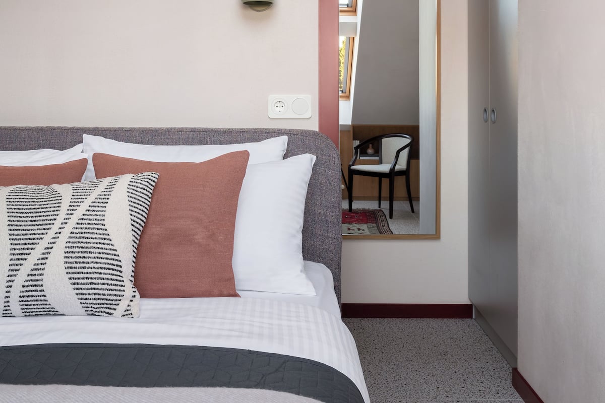 A neatly made bed with a variety of pillows and a headboard. A wall-mounted light fixture is visible above the bed.