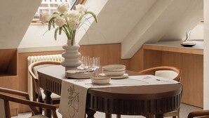 Un comedor con una mesa redonda, sillas, un florero con flores y un tragaluz.