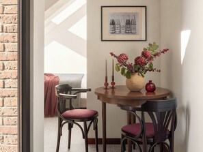 Ein Essbereich mit einem runden Tisch, zwei Stühlen, einer Blumenvase und einem gerahmten Bild an der Wand.