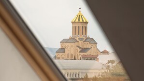 Vista enmarcada de un edificio con una cúpula y cruz destacadas, vista a través de una ventana con marco de madera.