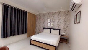 A bedroom with a bed, a nightstand, a wooden wardrobe, and a wall-mounted air conditioner. - Hotel Majesty inn (Jaipur)