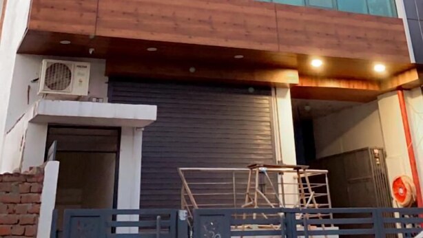 A modern building with large glass windows, a wooden facade, and a visible entrance with a metal gate. - Hotel Majesty inn (Jaipur)