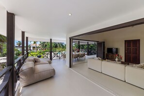 Uma sala de estar ampla com sofás, uma televisão e vista para uma varanda com mobiliário externo.