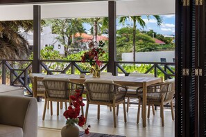 An outdoor dining area with a table and chairs, a vase with flowers, and a view of greenery and buildings.