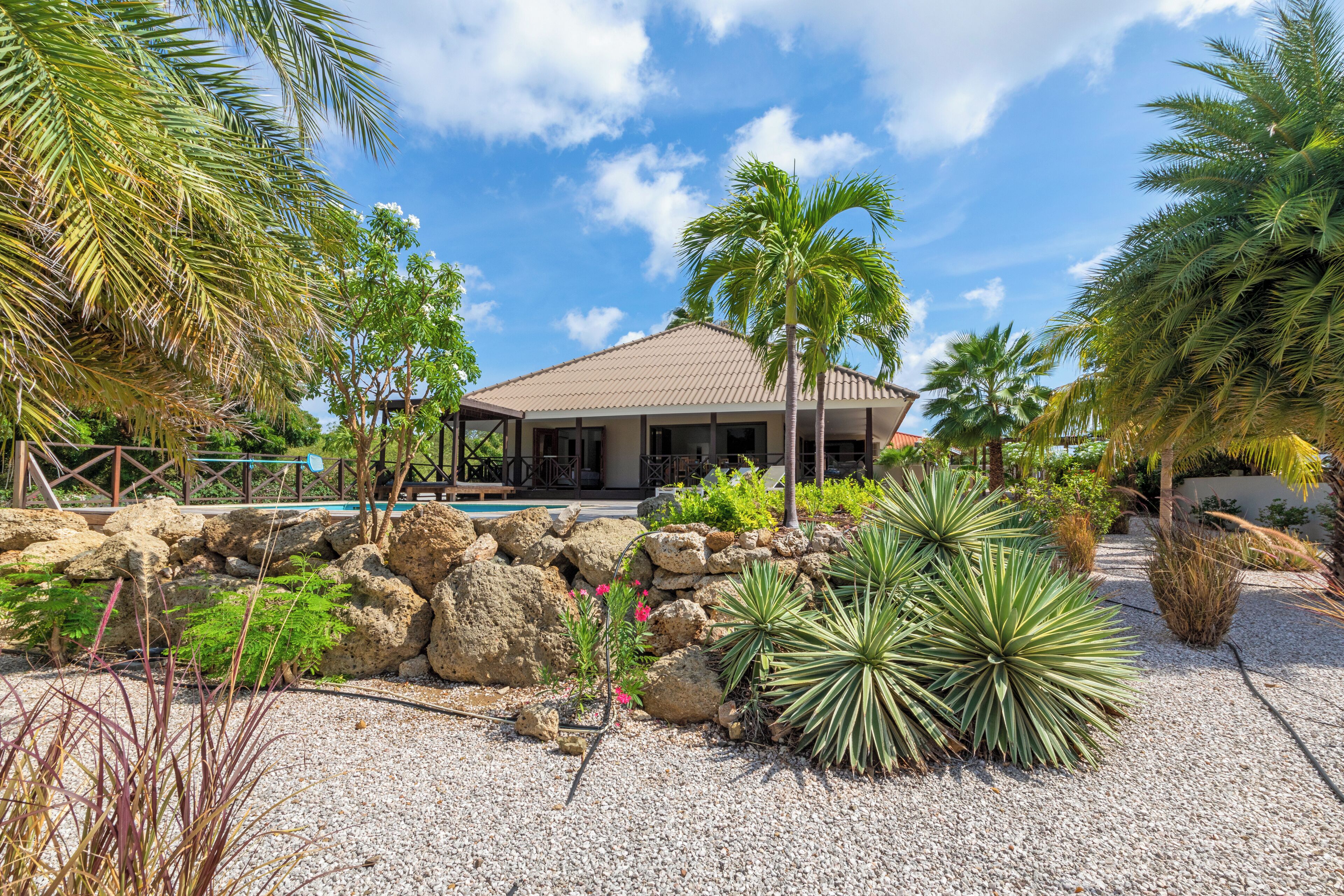 A house with a tiled roof, surrounded by a garden with palm trees and various plants.