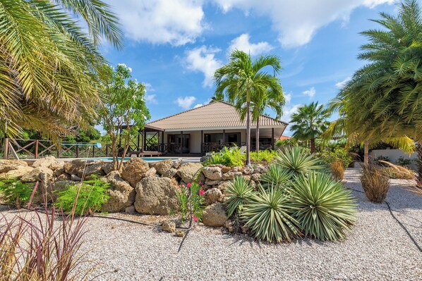 A house with a tiled roof, surrounded by a garden with palm trees and various plants.