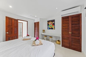 Una habitación de hotel con una cama grande, puertas de madera, un equipo de aire acondicionado y una obra de arte colorida en la pared.