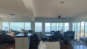 A spacious living area with a kitchen, dining table, and a large window overlooking the ocean. - Gorgeous beachfront house with stunning views, light and the sounds of the ocean (Manhattan Beach)