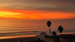 A sunset over the ocean with palm trees and buildings in the foreground. - Gorgeous beachfront house with stunning views, light and the sounds of the ocean (Manhattan Beach)