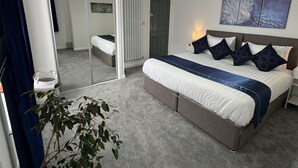 Ett modernt sovrum med en stor säng, ett sängbord, en spegel, en krukväxt och en dörr som leder till ett badrum.