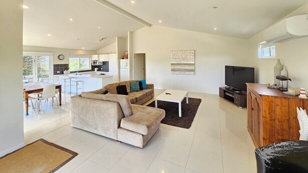 A spacious living area with a sofa, a coffee table, and a TV. There is a kitchen in the background with a dining area. - Tallara @ Robe - Stop and stay a while (Robe)