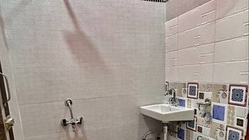 A bathroom with a white toilet, a sink, a red bucket, and patterned tiles.