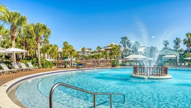 Una piscina con fuente, rodeada de palmeras y sillones de descanso.