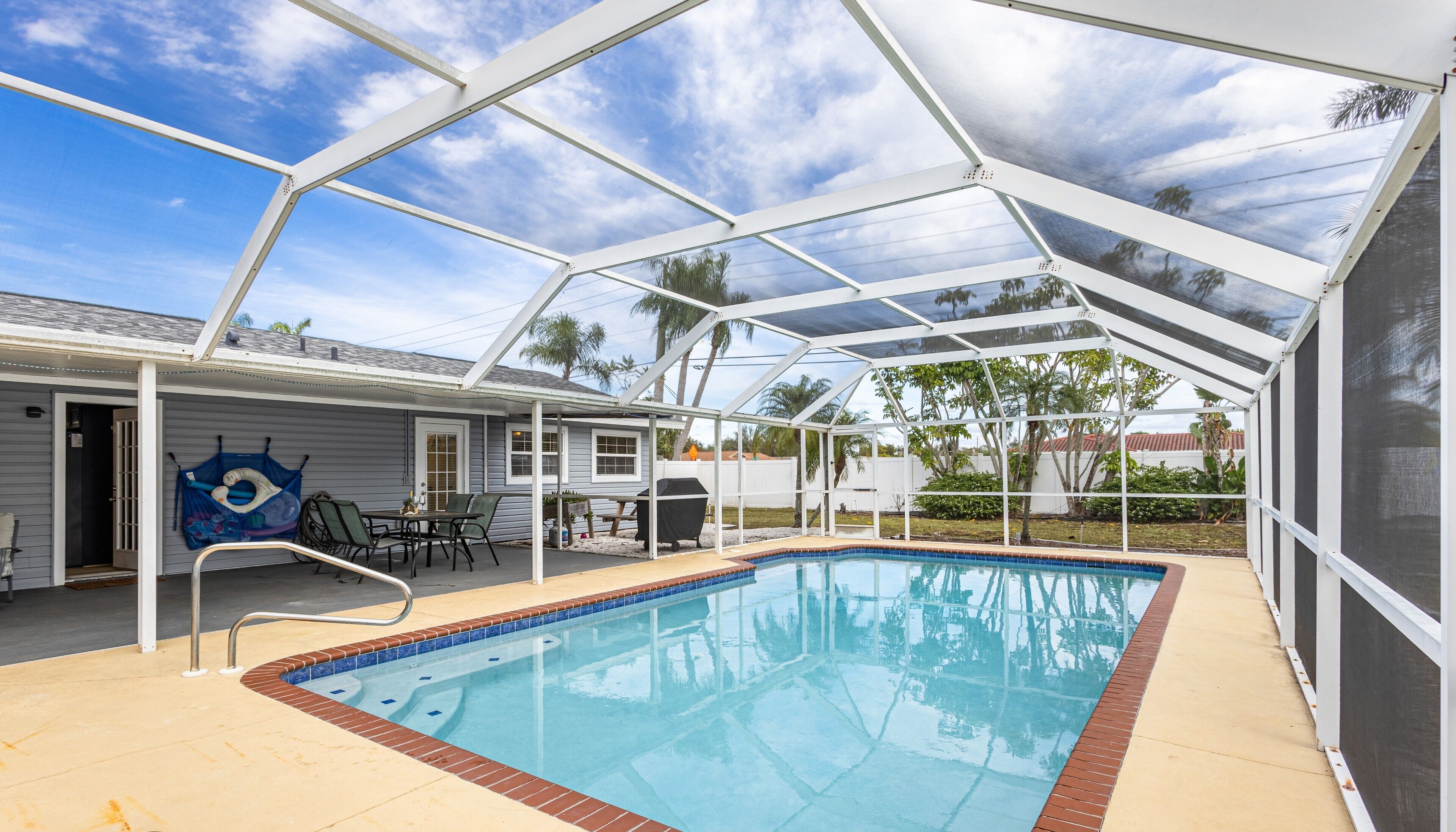 A covered outdoor swimming pool with a patio area, a grill, and a hammock.