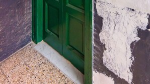 A green door with a red emergency exit sign, a textured wall, and a tiled floor.