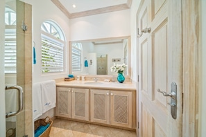 Une salle de bain avec un grand miroir, un lavabo et un meuble-vasque avec des placards. On y trouve également un porte-serviettes et un panier posé sur le sol.