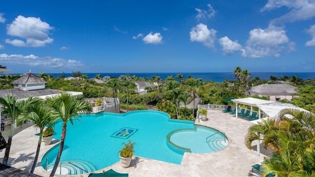 Zwembad van een resort met uitzicht op de oceaan, omringd door palmbomen en resortgebouwen.