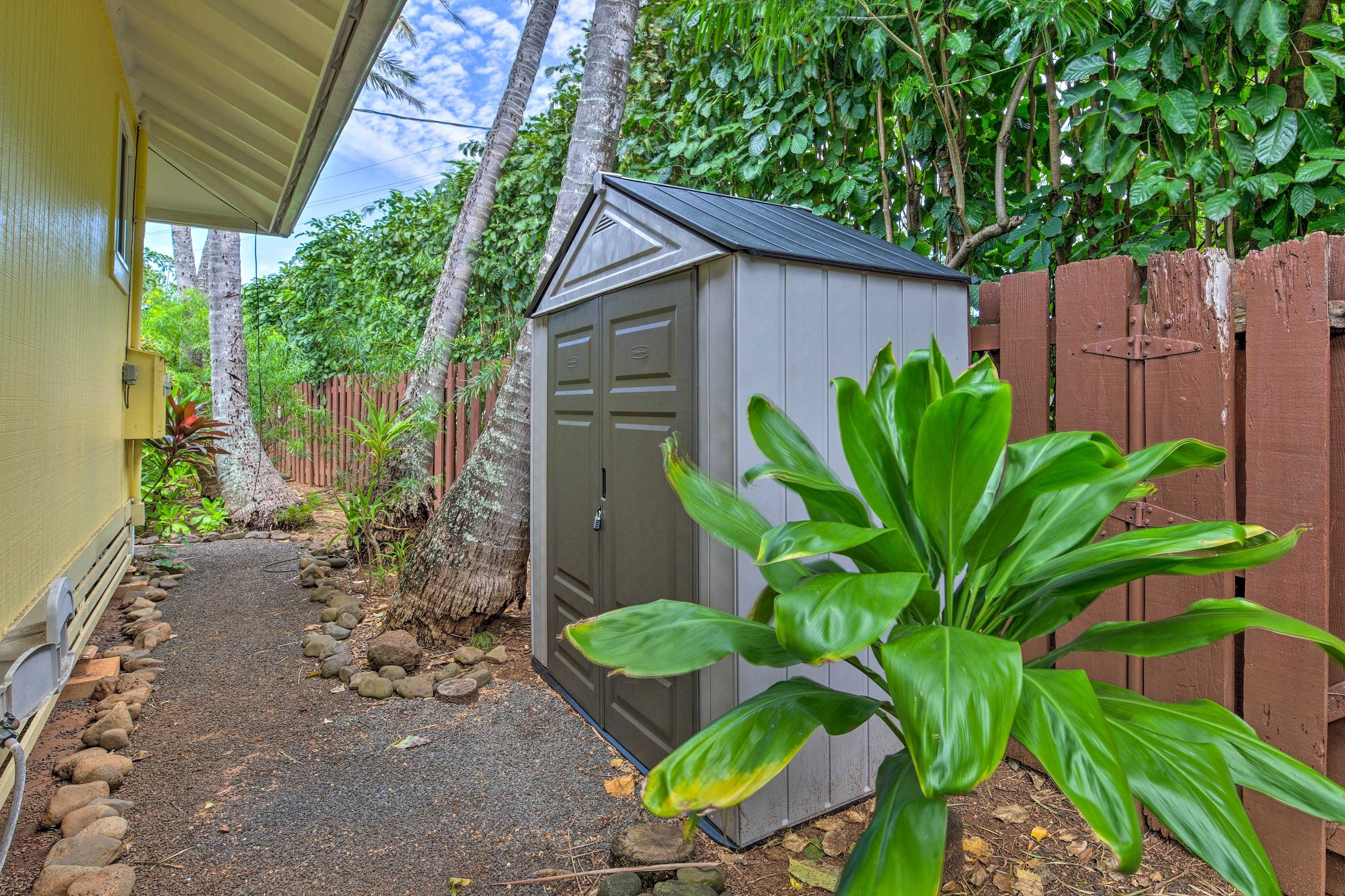 A small shed with a metal roof and a wooden door, surrounded by a garden with rocks and plants.
