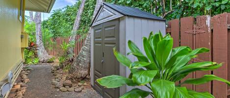 A small shed with a metal roof and a wooden door, surrounded by a garden with rocks and plants.