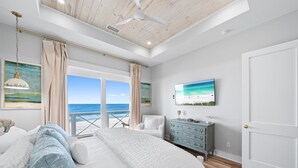 A bedroom with a large bed, a dresser, a TV, and a view of the ocean. - Blessing At Pier Park 6 Bedroom Home (Panama City Beach)