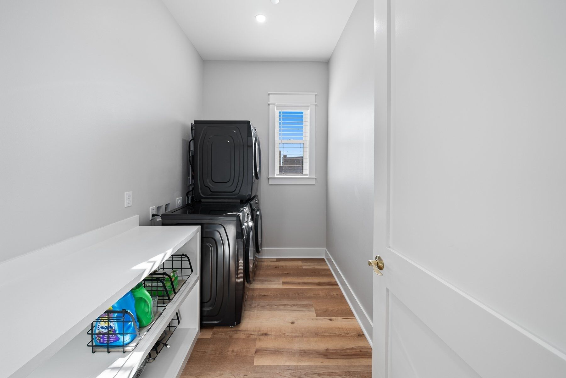 A narrow hallway with a washing machine and a shelf with dish soap.