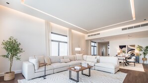 A modern living room with a sectional sofa, a coffee table, and a dining area with a lamp and table. - Sumptuous 5BR with Assist Rm in Al Dana Island, Sharm, Fujairah by Deluxe Holiday Homes (Fujairah)
