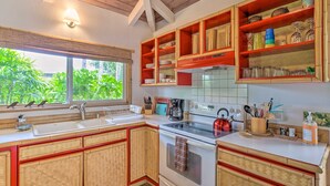 Une cuisine avec des meubles en bois, un fourneau et une fenêtre donnant sur un paysage verdoyant.
