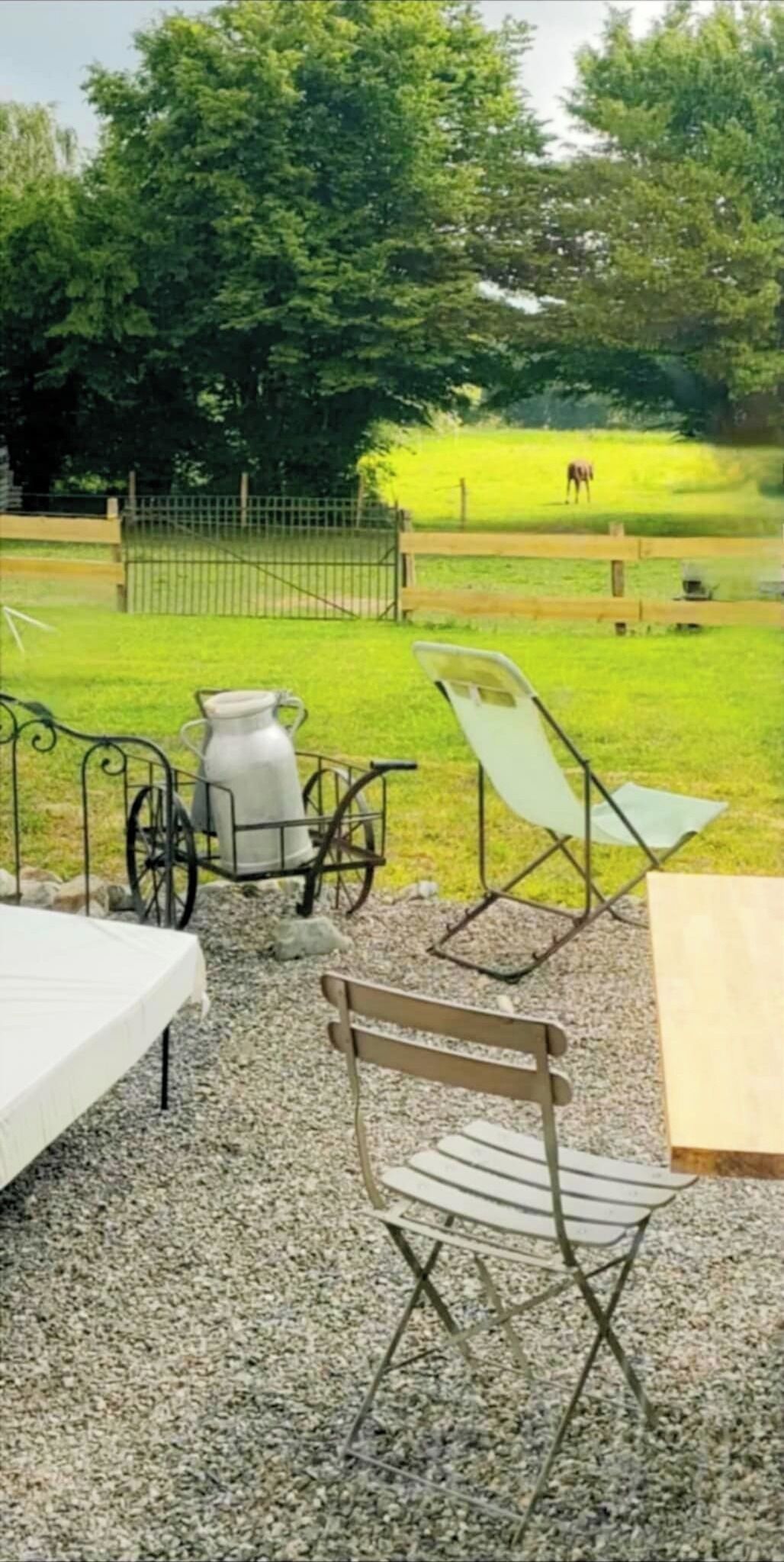 Uma área externa com assentos, uma cadeira de metal, uma mesa de metal e um jarro de leite de metal.