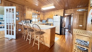 Ein Holzblockhaus-Interieur mit einer Küche, die eine zentrale Kochinsel, Barhocker und einen Kühlschrank beinhaltet.