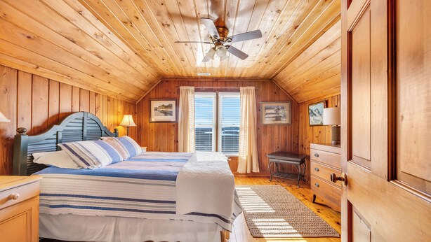 Ein gemütliches Schlafzimmer in einer Holzhütte mit einem Bett, Nachttischen, einer Kommode und einem Deckenventilator.