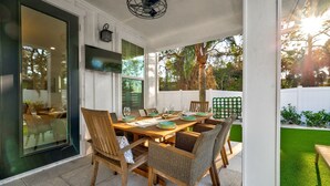 An outdoor patio with a wooden table set for dining, wicker chairs, and a view of the backyard.