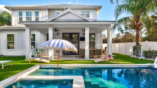 A poolside area with a pool, lounge chairs, and a covered seating area with a striped umbrella.