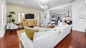 A spacious living room with a white sofa, wooden flooring, and a modern kitchen in the background.