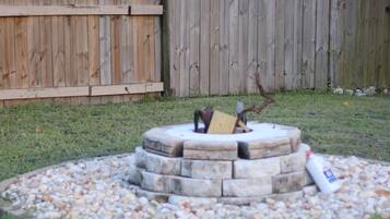 A circular stone fire pit surrounded by a gravel area, with a wooden fence in the background.