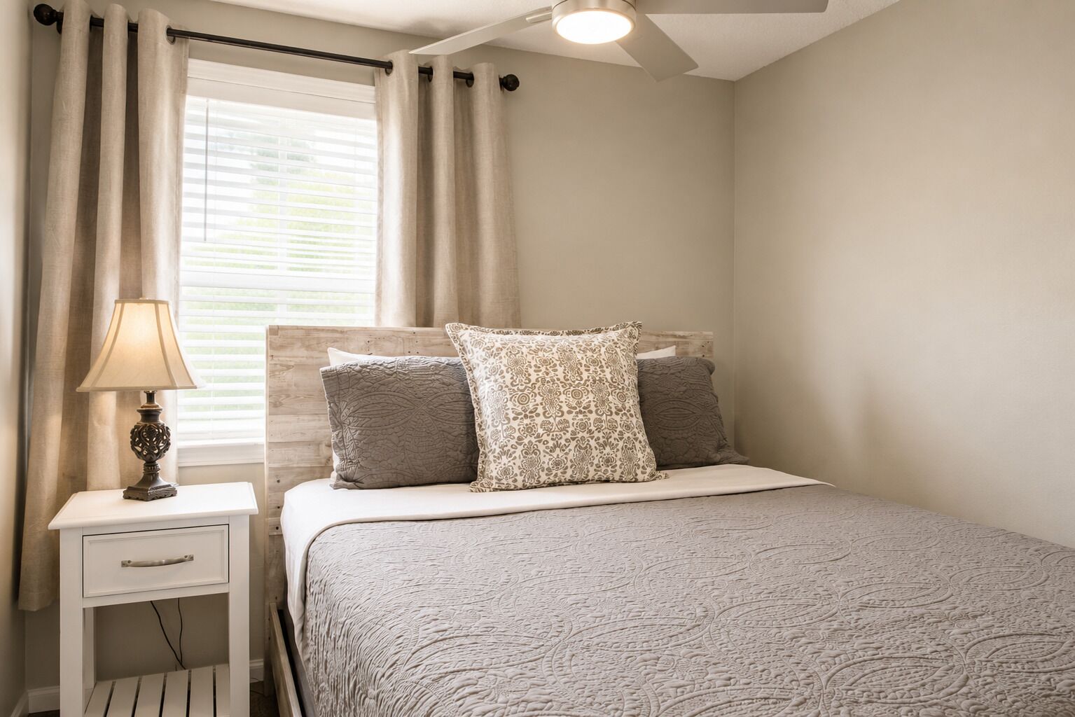 A bedroom with a bed, a nightstand, a lamp, and a window with curtains.