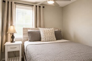 A bedroom with a bed, a nightstand, a lamp, and a window with curtains. - Your home away from home/The perfect place to unwind with family & Friends (New Port Richey)