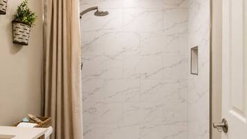 A bathroom with a shower, marble tiles, a wooden vanity, and a potted plant.