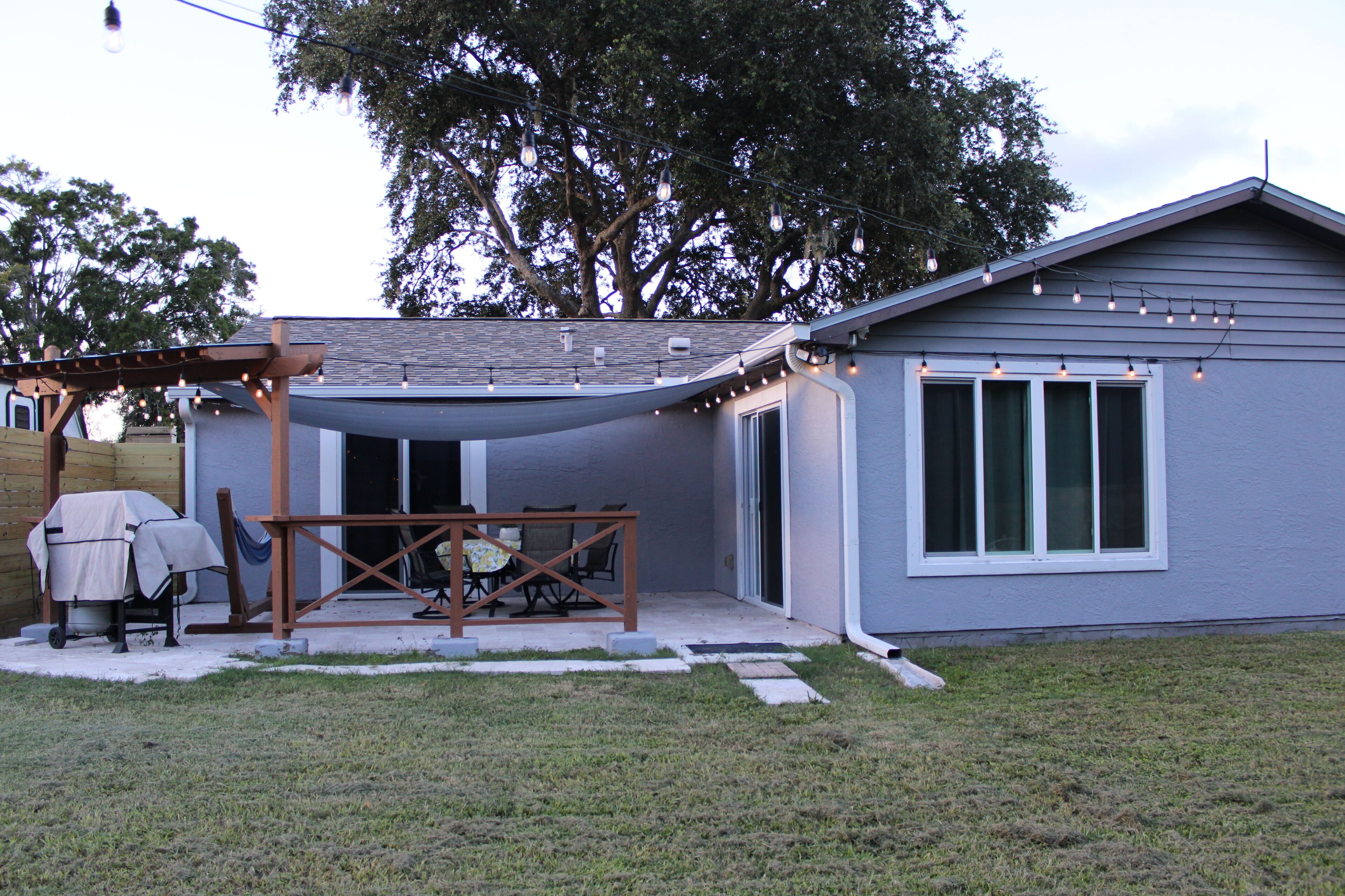A house with a covered patio, a barbecue setup, and a string of lights.