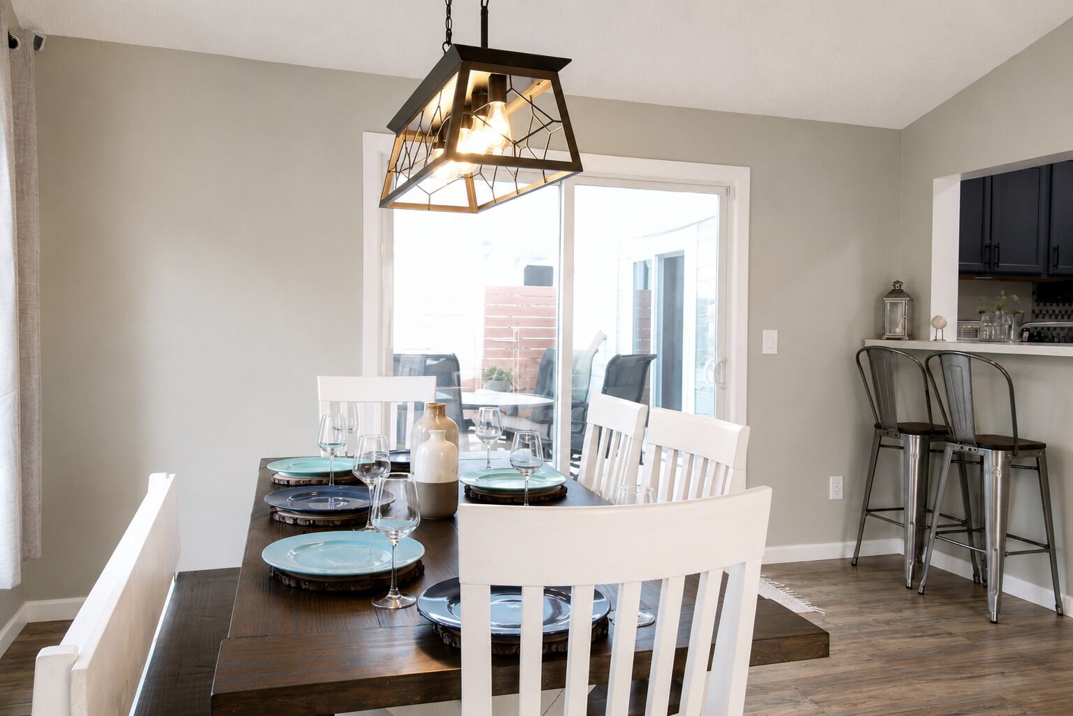 Een eetruimte met een houten tafel voor vier personen, witte stoelen en een hanglamp.