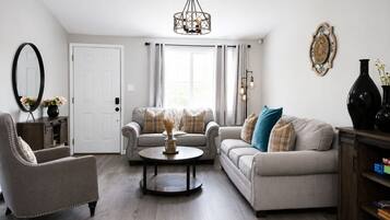 A living room with a sofa, armchair, and coffee table, a chandelier, and a door with curtains.