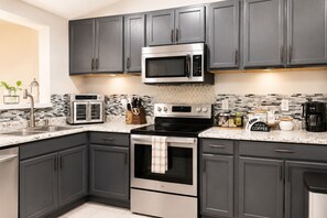A modern kitchen with dark cabinets, a stainless steel range, a microwave, and a coffee maker. - Your home away from home/The perfect place to unwind with family & Friends (New Port Richey)