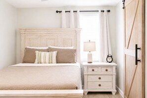 A bedroom with a bed, nightstand, lamp, clock, and a wooden wardrobe.