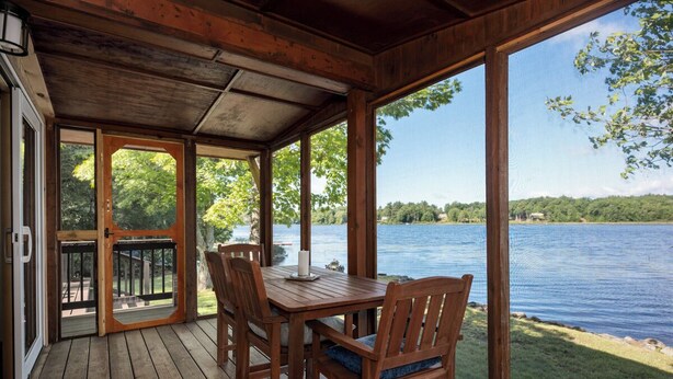 A wooden deck with a table and chairs overlooking a lake.