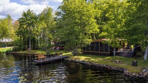 A lakeside property with a dock, outdoor seating, and a building with large windows overlooking the water.